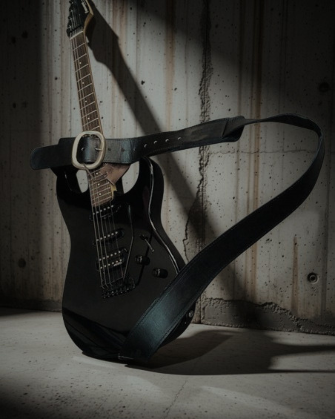 ACID · GAIA STRAPS en piel de vacuno negro, guitarra eléctrica apoyada en pared de hormigón